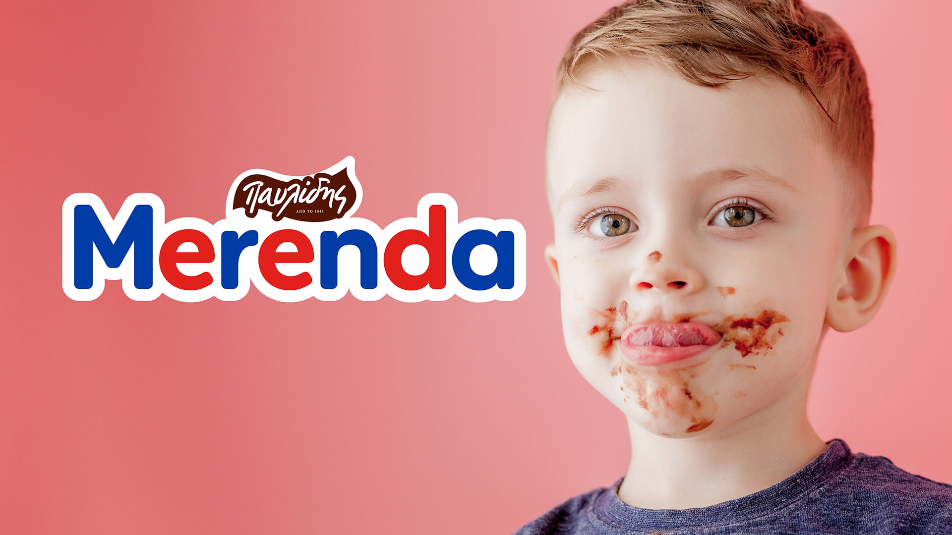 A young boy with Merenda chocolate spread all over his face, smiling at the camera, next to the redesigned Merenda (by Pavlidis) logo on a pink background.