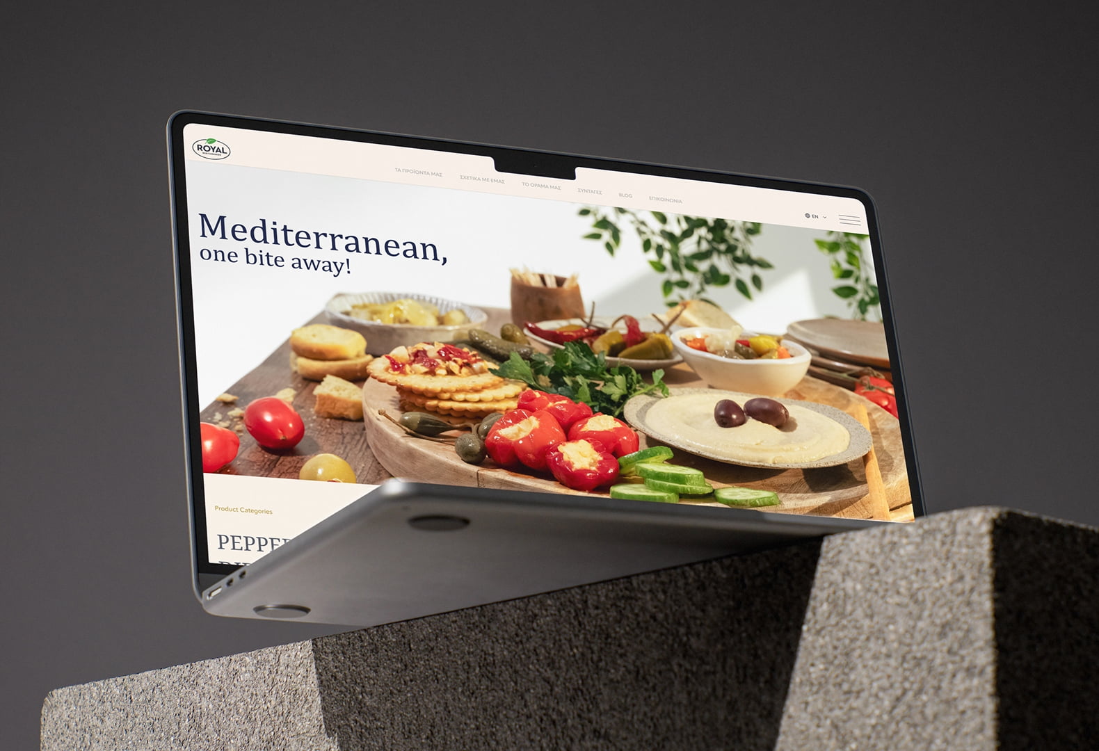 Dynamic angled laptop mockup resting on textured stone blocks, displaying the Royal Mediterranean website homepage and food photography hero banner, designed by 2yolk.