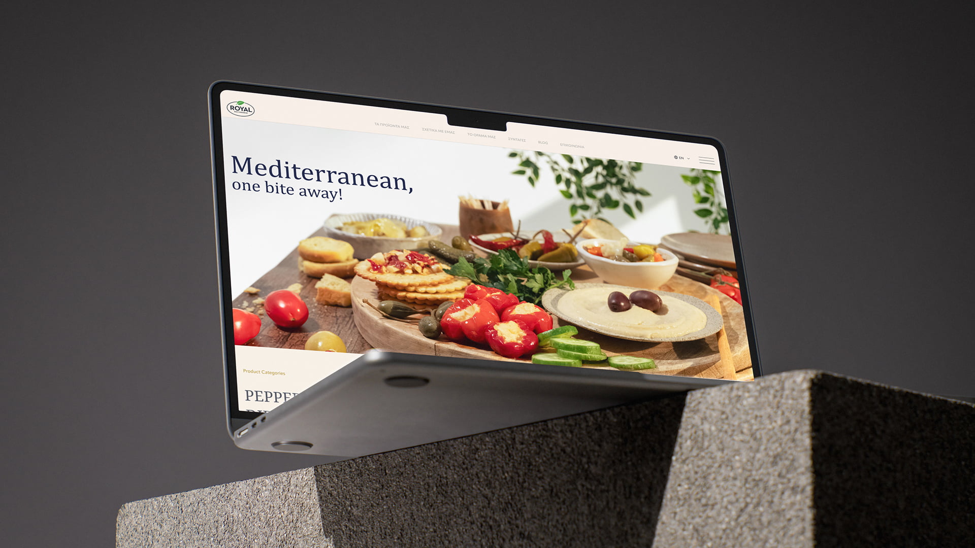 Dynamic angled laptop mockup resting on textured stone blocks, displaying the Royal Mediterranean website homepage and food photography hero banner, designed by 2yolk.