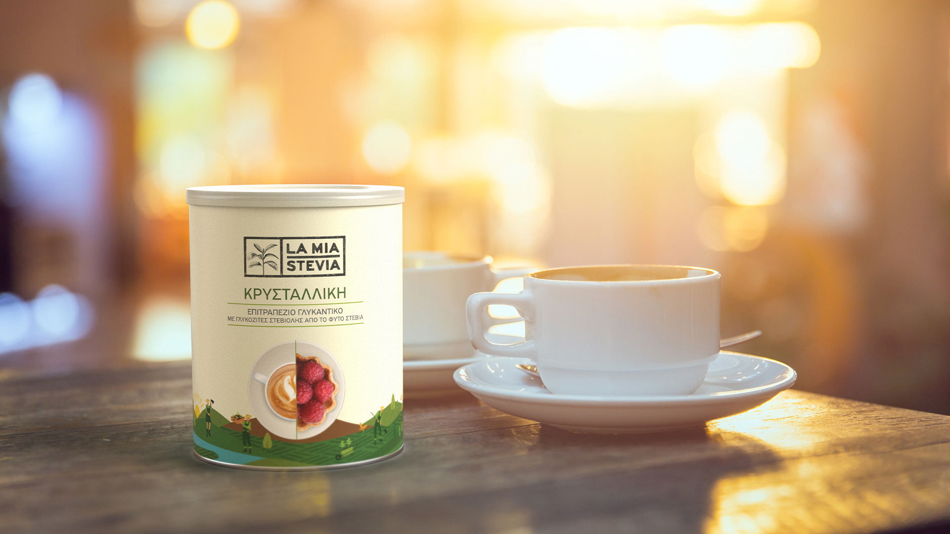 A tin of LA MIA STEVIA Crystalline sweetener (ΚΡΥΣΤΑΛΛΙΚΗ) on a wooden cafe table, next to a white cup of coffee, with a warm, blurred background.