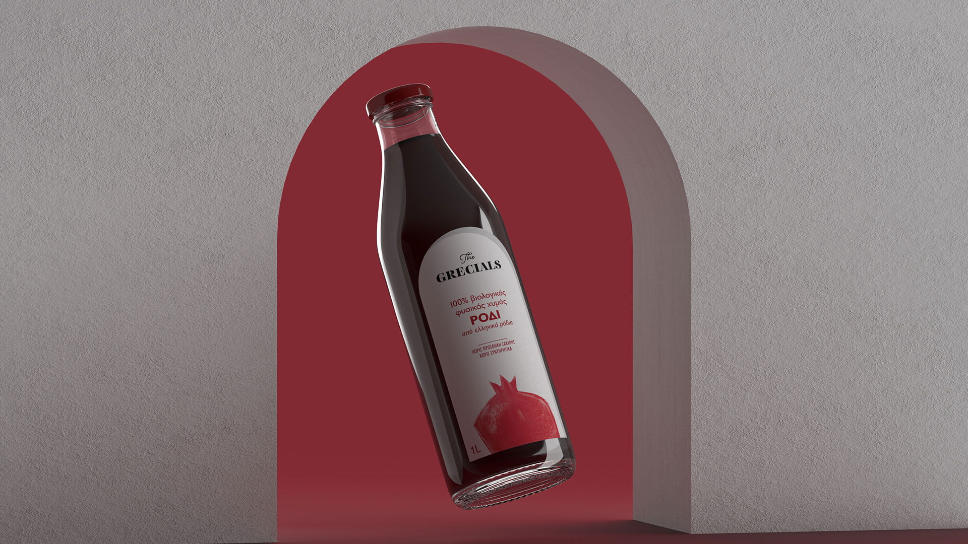 A glass bottle of The Grecíals Pomegranate Juice (ΡΟΔΙ), featuring a white label with a red pomegranate illustration, floating in a red archway against a grey background.