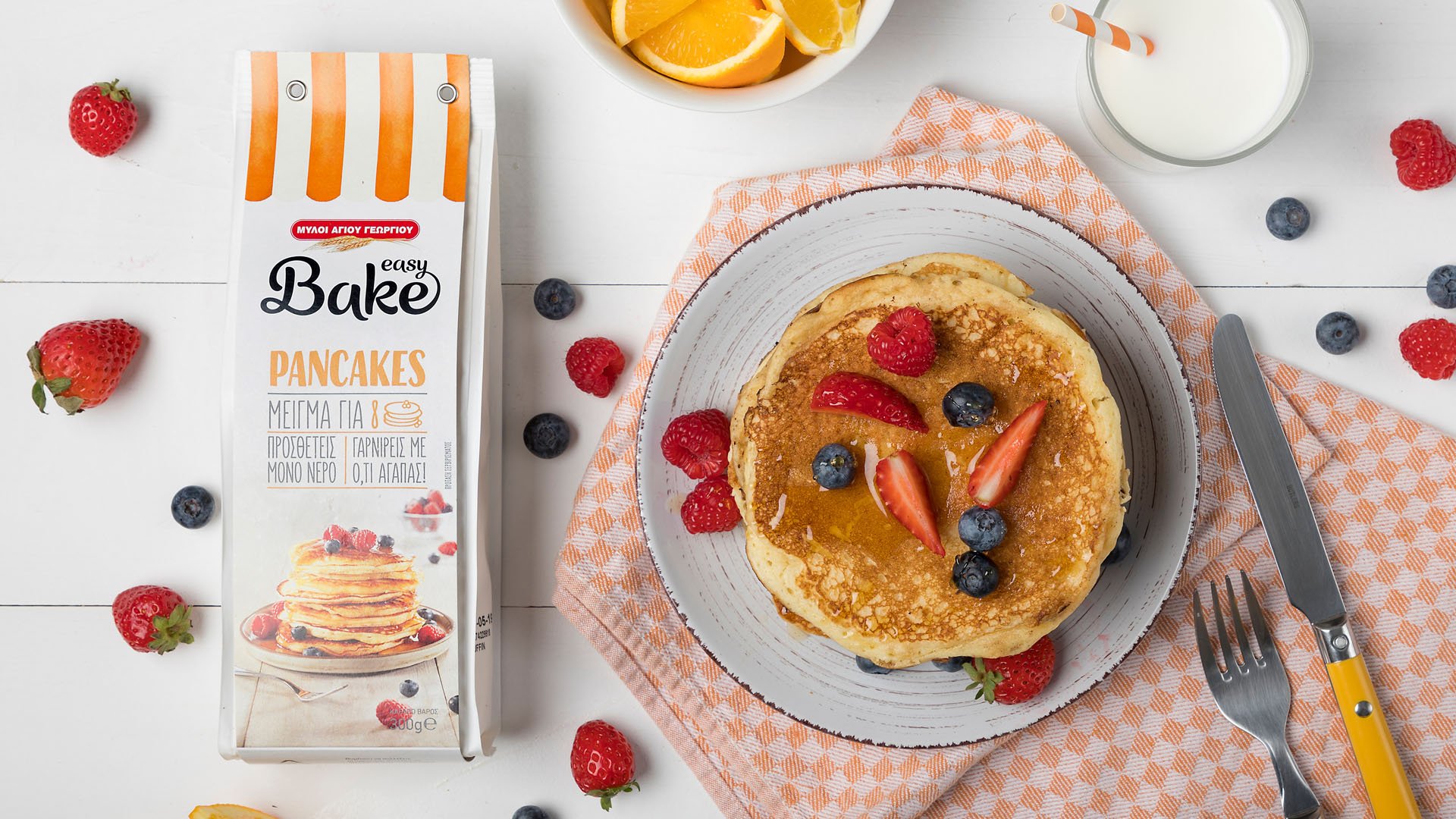 Food styling of pancakes topped by blueberries and strawberries next to Easy Bake pancake mix