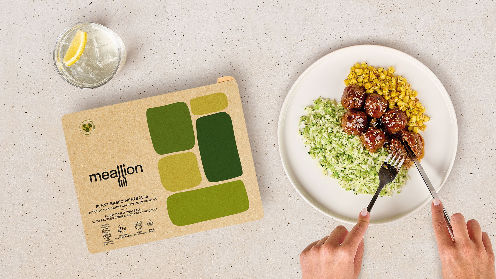 A flat lay showing the Meallion 'Plant-Based Meatballs' packaging next to a white plate with the prepared meal of meatballs, broccoli rice, and corn, with a person's hands eating.