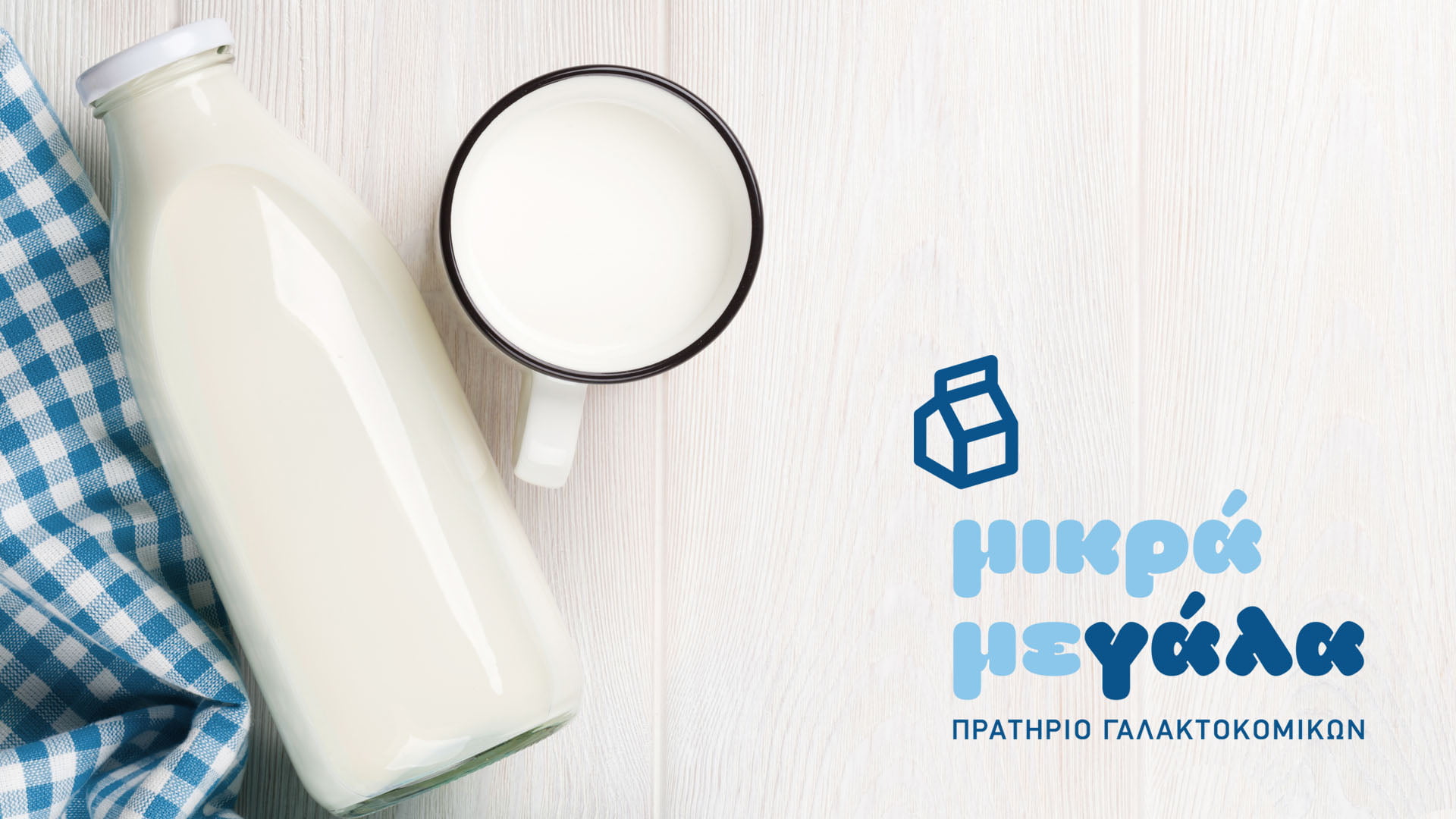 A flat lay of the "μικρά μεγάλα" (mikra megala) dairy store logo on a white wood background, next to a classic glass milk bottle, a white mug of milk, and a blue gingham napkin.
