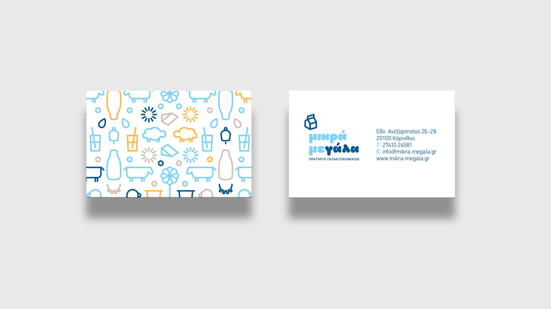A mockup of the "μικρά μεγάλα" (mikra megala) business card, showing the white side with the logo and contact details, and the other side with a colorful, playful pattern of dairy-themed illustrations.